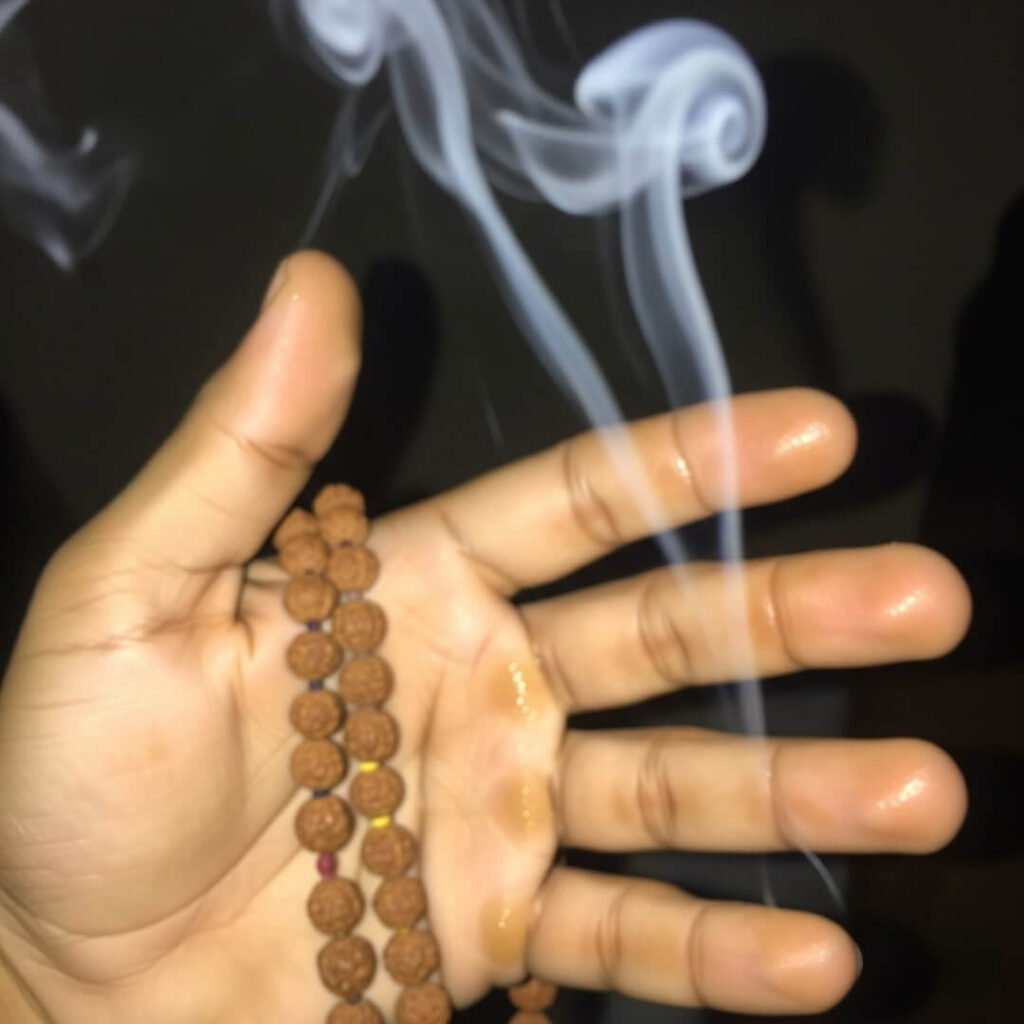 Chai-stained hands holding rudraksha mala and agarbatti smoke.