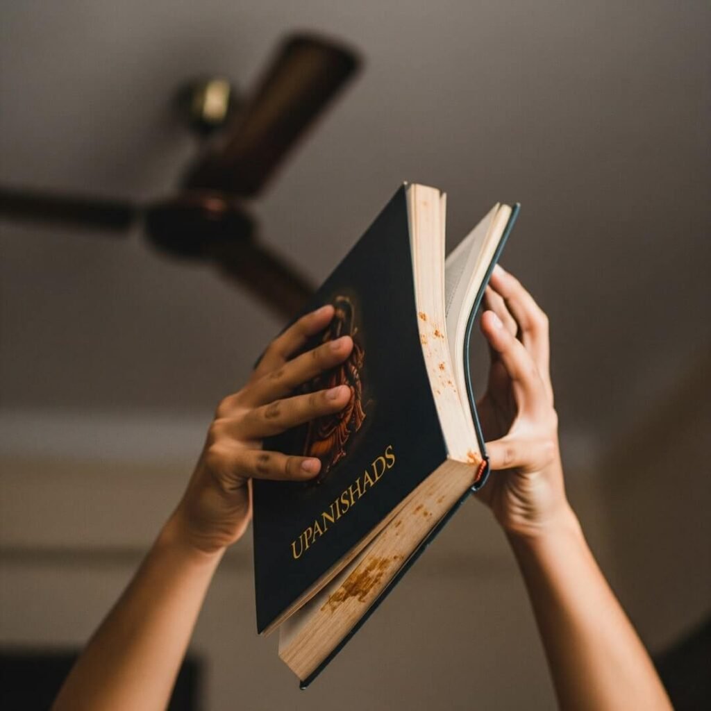 Hands holding an "Upanishads" book under a fan.